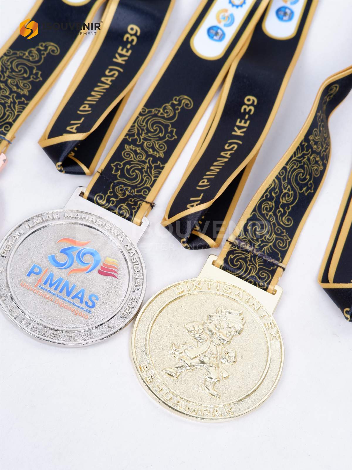 Medali Logam PIMNAS 2026 39th Universitas Diponegoro detail medali logam warna emas dengan relief figur dan tulisan melingkar serta pita hitam bermotif emas dengan logo acara